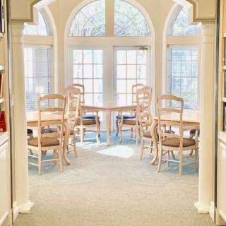 A bright dining area with arched windows letting in natural light, featuring a table and several chairs.