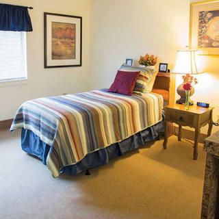A cozy bedroom with a single bed featuring striped bedding, accompanied by a nightstand and lamp.