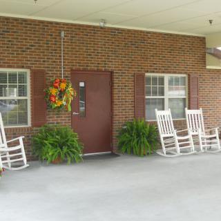 A cozy porch with white rocking chairs and decorative plants against a brick wall.