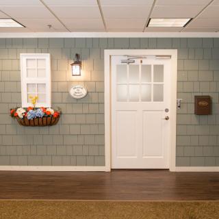 A welcoming interior setup featuring a door and window, accented with a basket of artificial flowers and a wall-mounted lamp.
