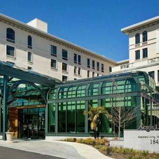 A modern hospital building featuring a glass entrance structure under a clear blue sky.