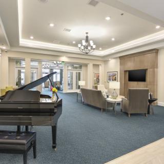 A spacious and elegantly designed living room featuring a grand piano, comfortable seating, and a modern chandelier.