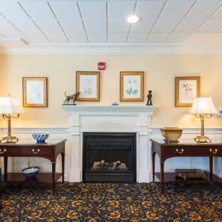 A cozy living room with a central fireplace flanked by two tables and lamps, adorned with framed artwork on the wall.
