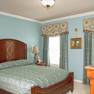 A traditional-style bedroom with blue walls, matching bedspread and curtains, wooden furniture, and decorative elements.