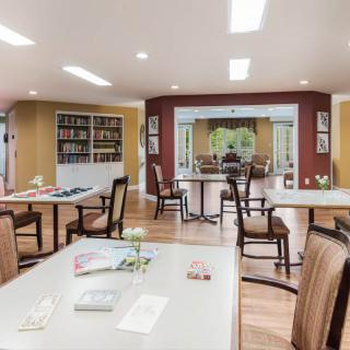 A spacious community dining area with tables, chairs, and bookshelves, providing a cozy and welcoming atmosphere.