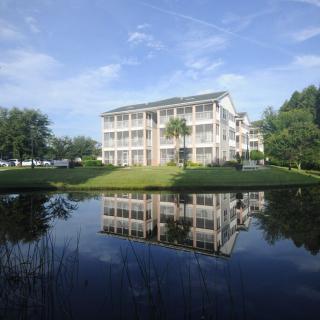 A serene view of a white building reflected in a calm pond surrounded by greenery.
