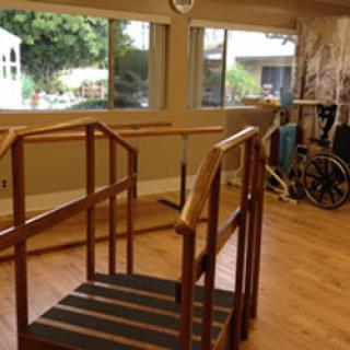A physical therapy space featuring a wooden ramp and railings, designed to assist individuals in rehabilitation.