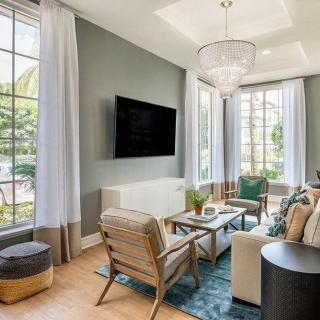 A modern living room with large windows, stylish furniture, and a flat-screen TV.