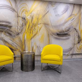 A modern waiting area featuring bright yellow chairs, a metallic table, and an abstract wall mural.
