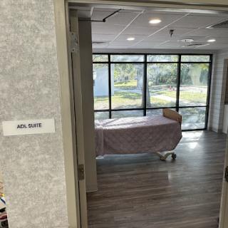 A view into a hospital patient room featuring a bed and large windows providing natural light.