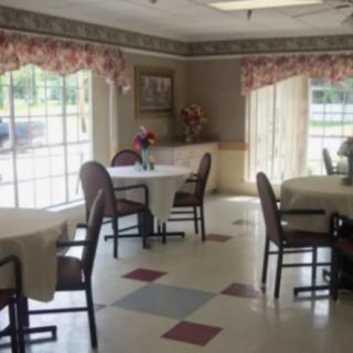 A well-lit dining area with tables and chairs, featuring large windows and floral curtains.