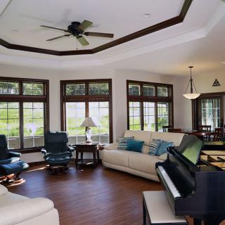 Spacious living room with large windows, comfortable seating, and a piano.