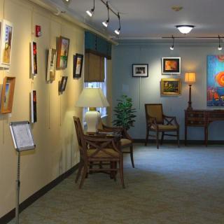 Interior view of an art gallery with paintings displayed on the walls and cozy seating arrangements.