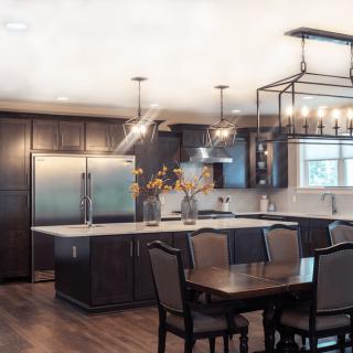 A modern kitchen with dark cabinets and a spacious island, featuring pendant lights and an adjacent dining area.