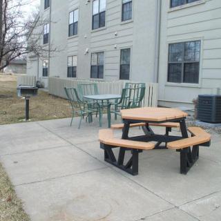 An outdoor patio area with a picnic table, chairs, and a grill next to a building.