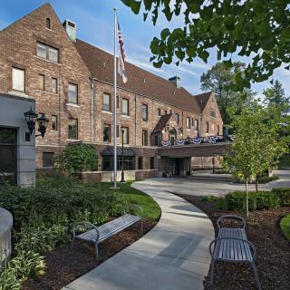 A brick building with a sloped roof, surrounded by greenery and benches along a winding pathway.