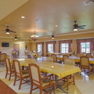 A spacious dining area with multiple tables and chairs, illuminated by ceiling lights and natural light from large windows.