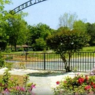 A scenic view of a garden with colorful flowers, a black fence, and lush green trees in the background.