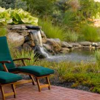 A tranquil garden scene with chairs overlooking a small waterfall and pond.