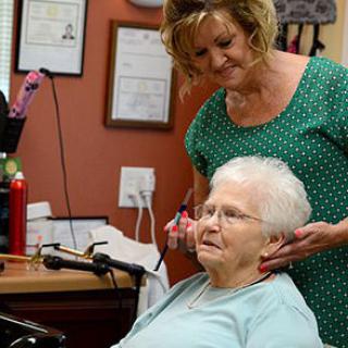 A hair stylist provides a haircut to an elderly woman in a salon.