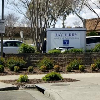 Entrance sign for Bayberry, surrounded by greenery and vehicles.