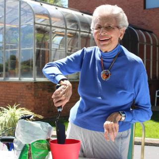 An elderly woman happily gardening outside on a sunny day.