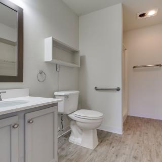 A modern bathroom interior featuring a toilet, sink, and mirror with light wood flooring.