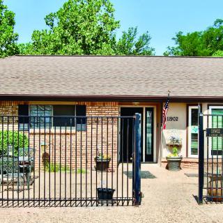 A single-story brick house with a fenced front yard and surrounding trees.