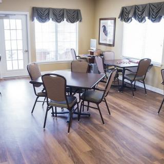 A bright dining area with tables and chairs, featuring hardwood floors and large windows.