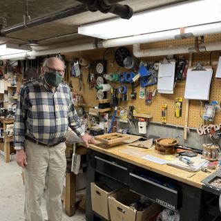 A person standing in a woodworking workshop surrounded by tools and materials.