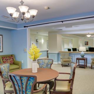A cozy living and dining area featuring comfortable seating, a wooden table, and a chandelier under soft blue walls.