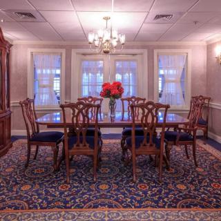 A formal dining room with an elegant wooden table and chairs, a chandelier overhead, and decorative flowers on the table.