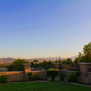 A serene landscape with a view of mountains under a clear evening sky, framed by trees and a stone fence.
