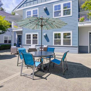 A sunny patio with a table, chairs, and a large umbrella outside a blue house.