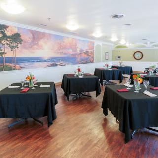 A cozy restaurant setting featuring tables adorned with black tablecloths and decorative centerpieces, complemented by a beautiful mural on the wall.