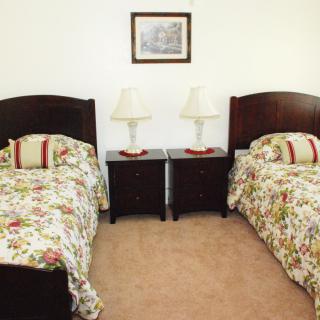 A cozy bedroom featuring twin beds with floral bedding, flanked by nightstands and lamps, and a painting on the wall.