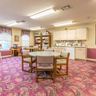 A cozy interior room featuring a round table with chairs, surrounded by bookshelves and a small kitchen area.
