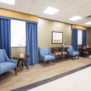 A cozy waiting room with blue chairs and curtains, featuring artwork on the wall.
