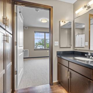 A modern bathroom with wood cabinetry and a view into the adjoining room.