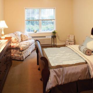 A cozy bedroom with a bed, sofa, and a window letting in natural light.
