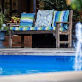 A cozy outdoor bench with colorful cushions by a bright blue swimming pool.