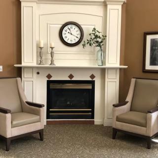 A cozy living room setting featuring a fireplace with two armchairs and a clock above the mantelpiece.