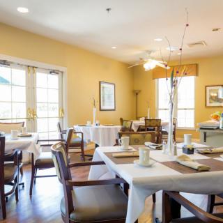 A cozy dining area with neatly arranged tables and chairs, featuring large windows that let in ample natural light.