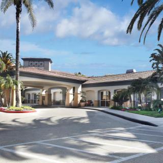 A large building with palm trees and a driveway under a blue sky with clouds.
