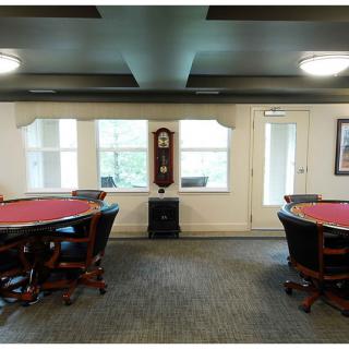 A well-lit game room featuring two poker tables and a grandfather clock.