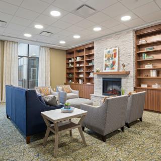A modern living room features a cozy seating area with sofas and chairs around a fireplace, surrounded by bookshelves.