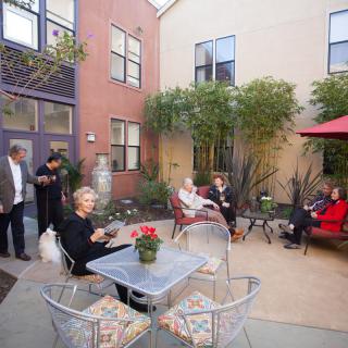 A group of people enjoying a gathering on a cozy outdoor patio with seating and a red umbrella.