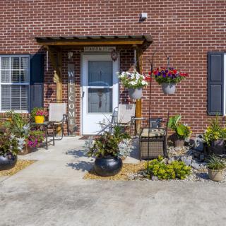 A welcoming front porch with potted plants and outdoor seating against a brick wall.