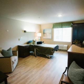A well-furnished hospital room with a bed, seating area, and large window.