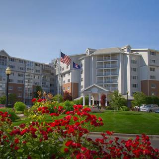 A residential building surrounded by a garden with red flowers and flags waving in front.
